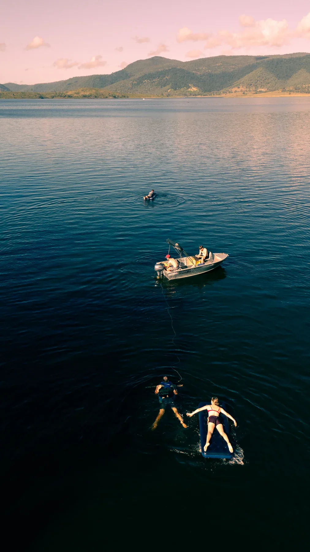 Swimmers floating beside a small boat on Lake Somerset, with pink clouds over the hills